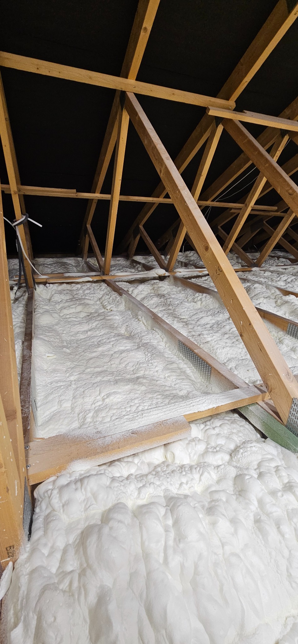 Poddasze z drewnianą konstrukcją wypełnione białą pianką PUR, widok z dołu. Izolacja natryskowa w trudno dostępnym miejscu.