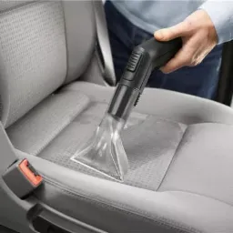 Czyszczenie tapicerki samochodowej odkurzaczem piorącym z przezroczystą końcówką, widoczne ślady wilgoci na fotelu.