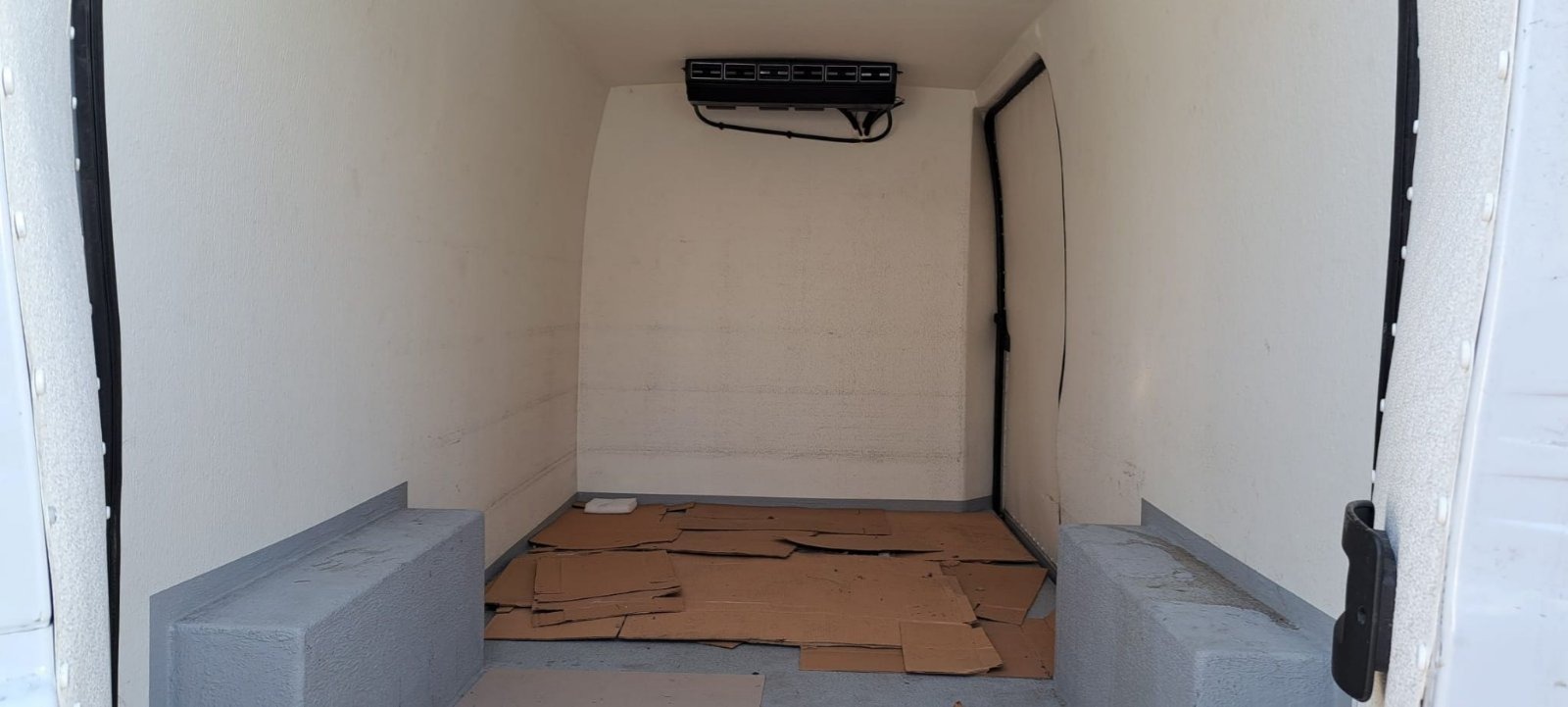 Wnętrze chłodni samochodu dostawczego, z widoczną jednostką chłodzącą pod sufitem i kartonami na podłodze, przygotowane do transportu.