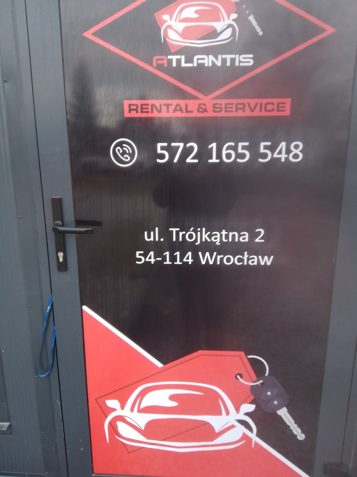 Drzwi z grafiką firmy oferującej wynajem i serwis samochodów, widoczny numer telefonu i adres we Wrocławiu.