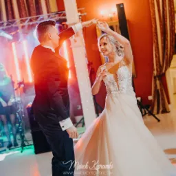 Para młoda tańczy pierwszy taniec podczas wesela, widoczny zespół muzyczny i oświetlenie sceniczne.