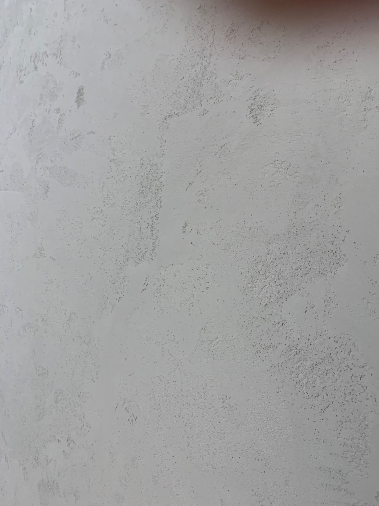 Szara ściana z delikatną, nieregularną fakturą, przypominającą efekt dekoracyjnego tynku.