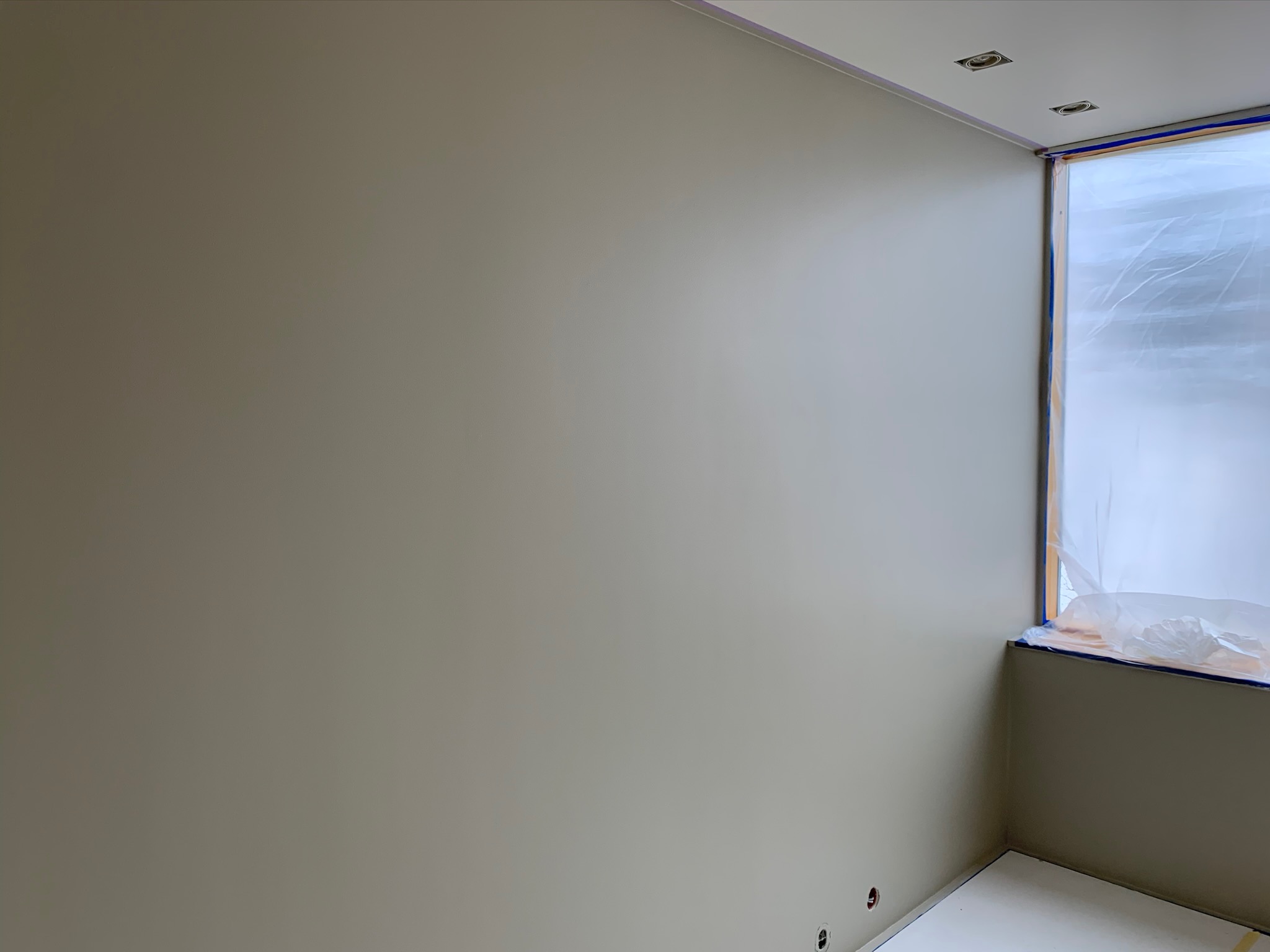 Świeżo pomalowane na szaro ściany pokoju, okno zabezpieczone folią malarską, widoczne puszki elektryczne