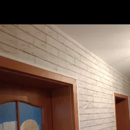 Ściana wykończona dekoracyjną, białą okładziną imitującą cegłę, z widocznymi drewnianymi futrynami drzwi.