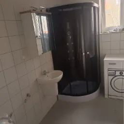 Nowoczesna łazienka z kabiną prysznicową z hydromasażem, umywalką na postumencie i pralką z minimalistycznym wzorem na szafce, wykończona białymi płytkami.