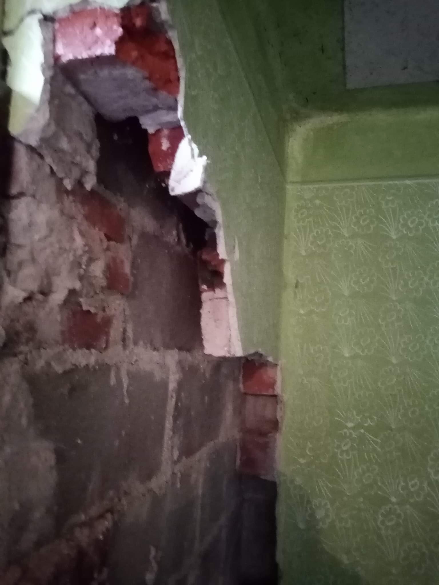 Odkryta ceglana ściana z fragmentami starego tynku i zielona ściana z wzorzystą tapetą, ukazująca stan przed remontem.