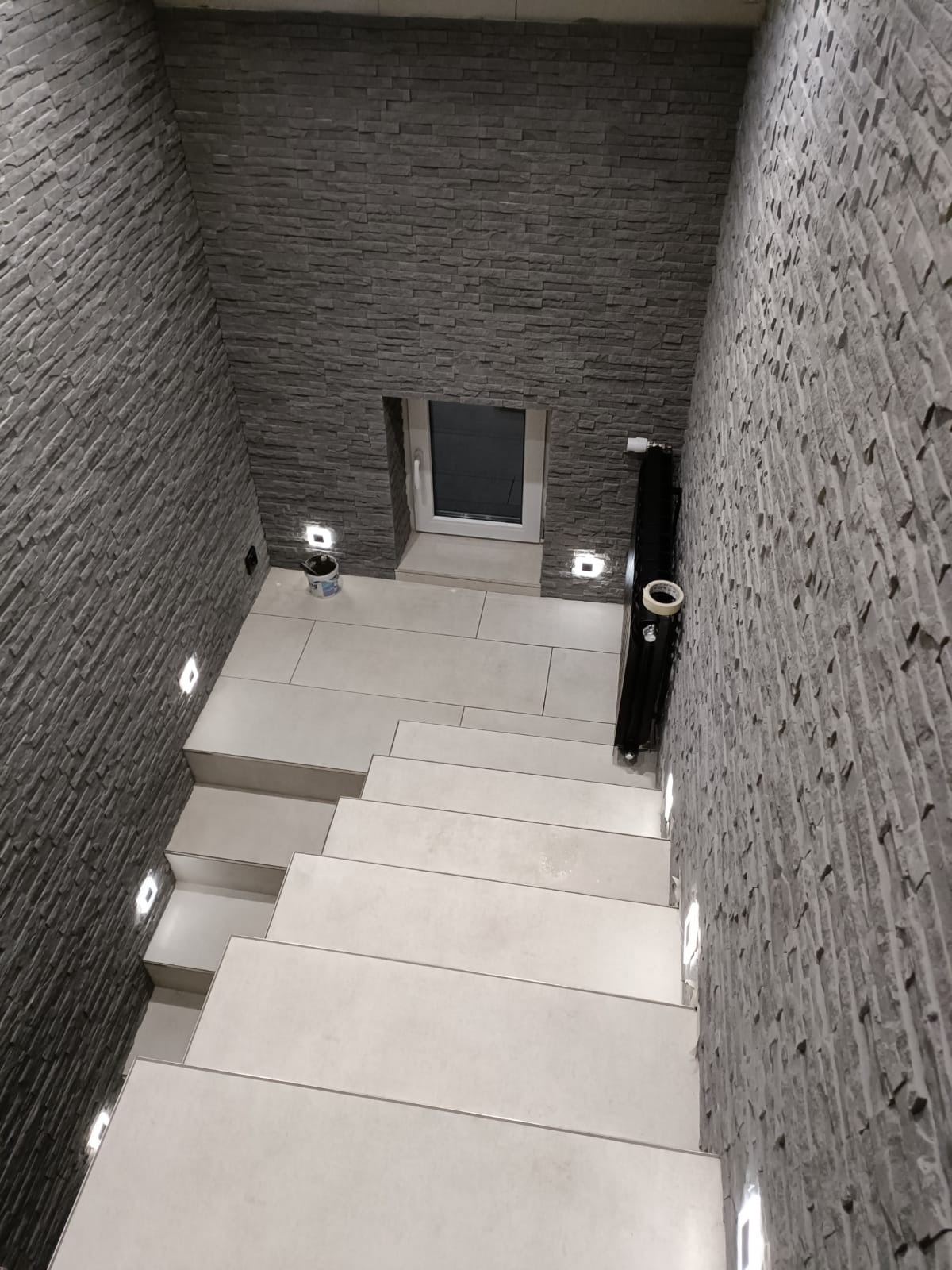 Klatka schodowa wykończona płytkami imitującymi kamień, z podświetlanymi stopniami i oknem na podeście, widok z góry.