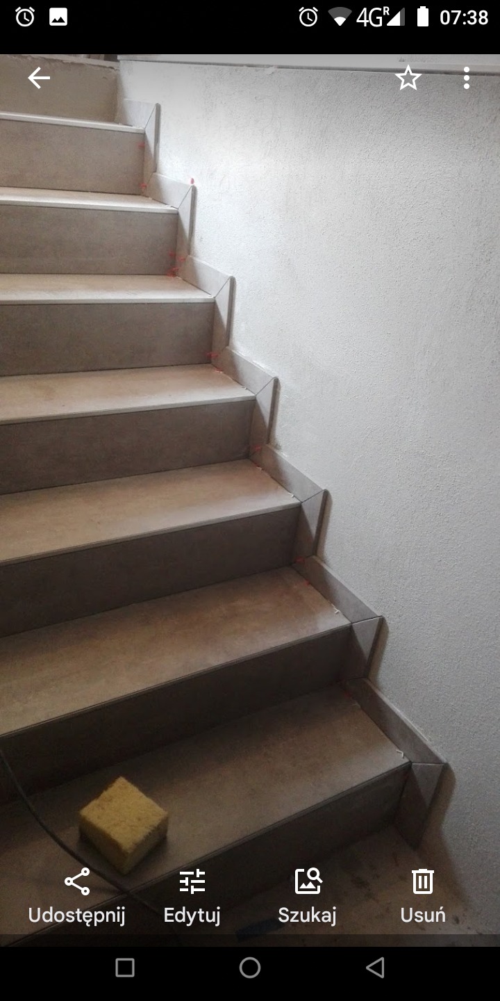 Wyłożone płytkami schody wewnętrzne z żółtą gąbką na dole, widoczne małe czerwone krzyżyki dystansowe między płytkami.