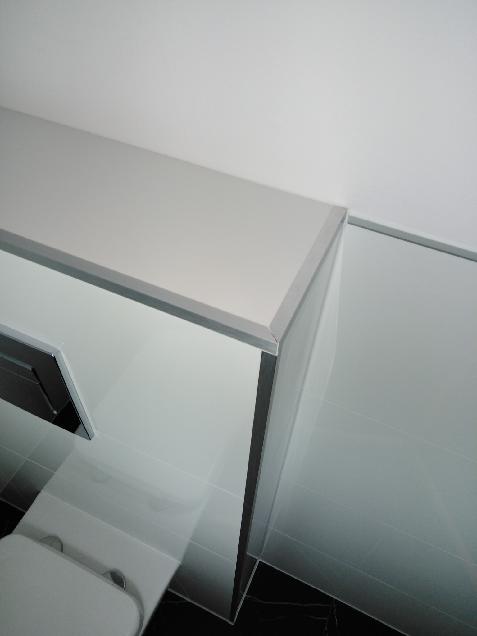 Nowoczesna kabina prysznicowa z białymi, błyszczącymi płytkami i czarną marmurową podłogą, widok z góry, minimalizm.