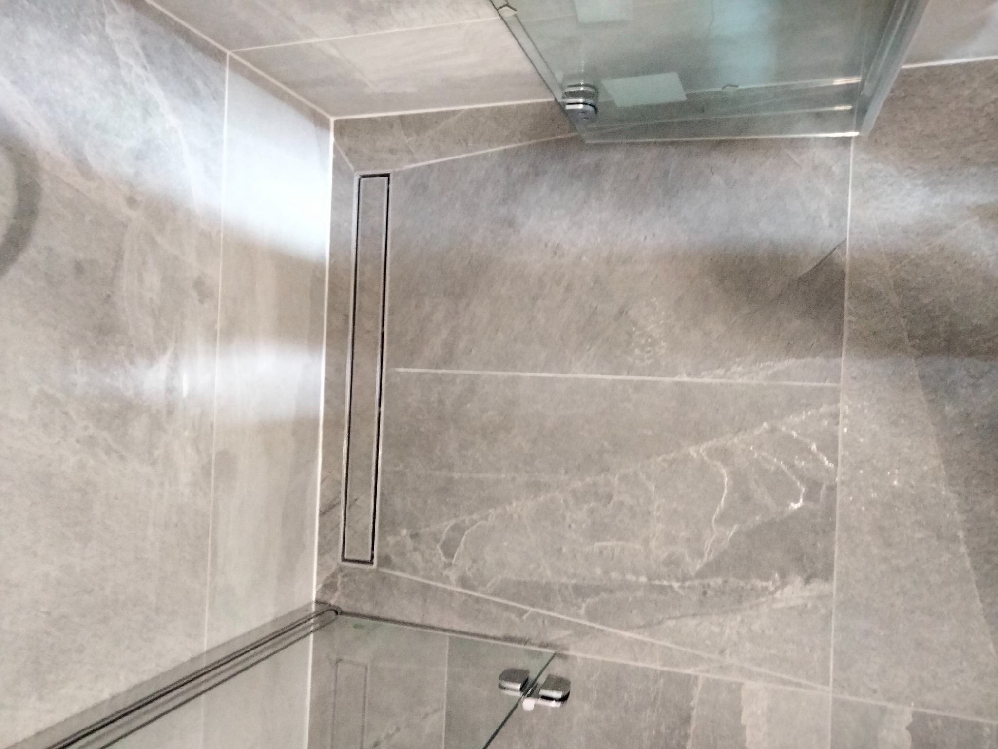 Szare płytki imitujące marmur w kabinie prysznicowej z odpływem liniowym i szklanym panelem