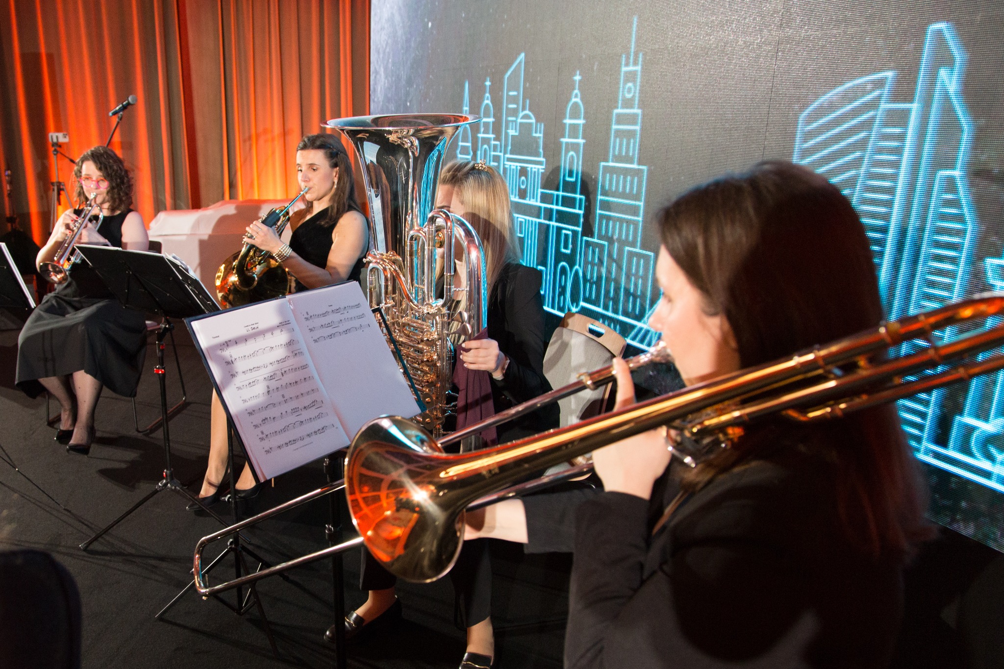 Kwartet instrumentalny grający na scenie z podświetlanym tłem przedstawiającym abstrakcyjny pejzaż miejski w neonowych barwach.