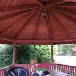 Drewniana altana z widokiem na zieleń, wewnątrz krzesło, stolik i kwiaty, dekoracja pod dachem w kształcie kuli.