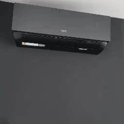 Czarny klimatyzator AUX zamontowany na ciemnoszarej ścianie w pomieszczeniu z białym sufitem i okrągłym oświetleniem punktowym.