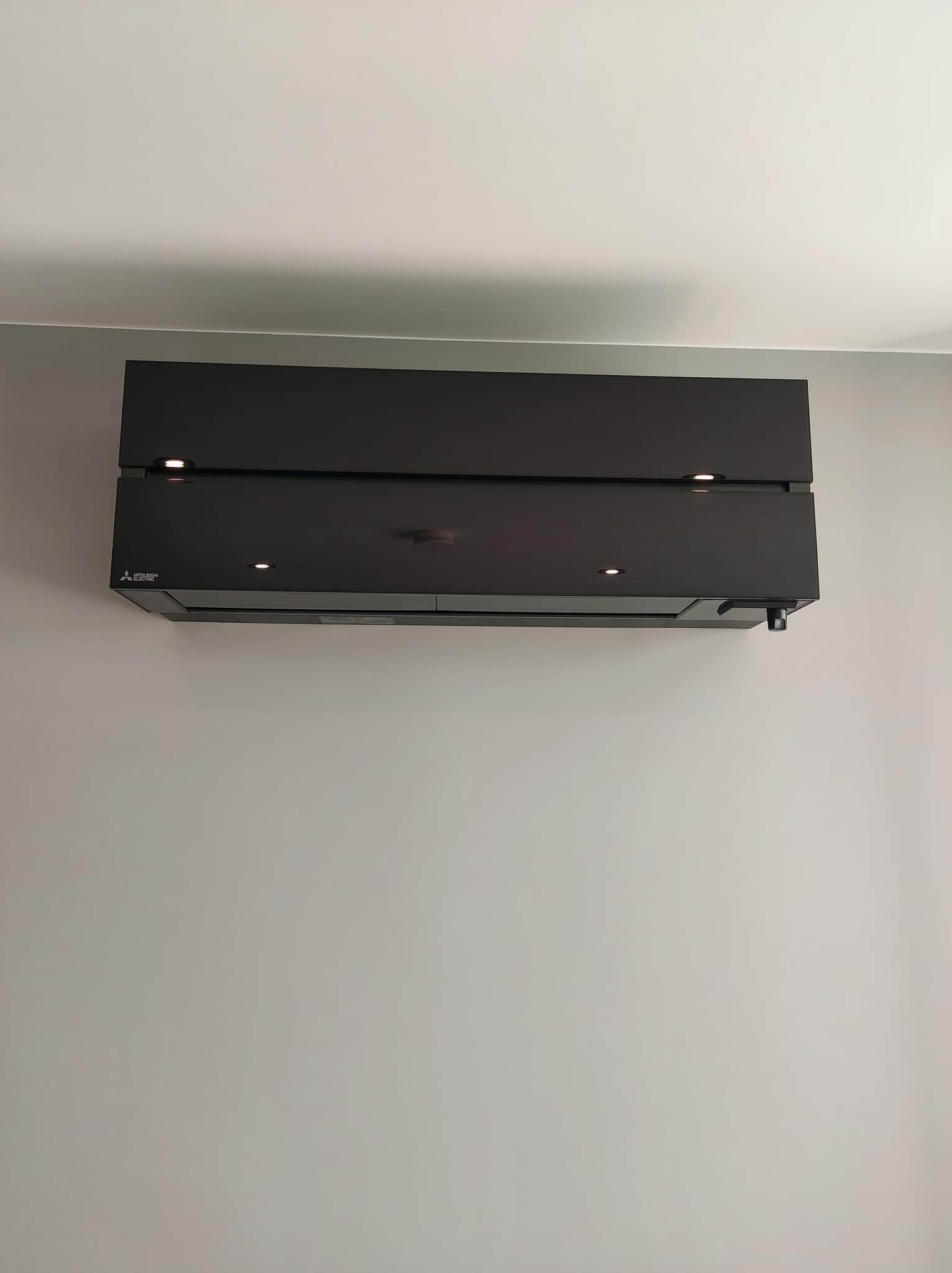 Czarna jednostka klimatyzacji Mitsubishi Electric zamontowana na szarej ścianie, z widocznymi punktowymi światłami LED.