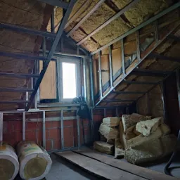 Poddasze w trakcie adaptacji: widoczne ocieplenie wełną mineralną, metalowy stelaż konstrukcyjny, ceglana ściana i skosy dachu z oknem.