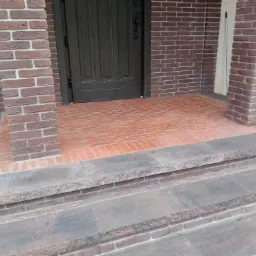 Wykończone wejście do domu z ceglaną elewacją i schodami wyłożonymi płytami z szarego kamienia.