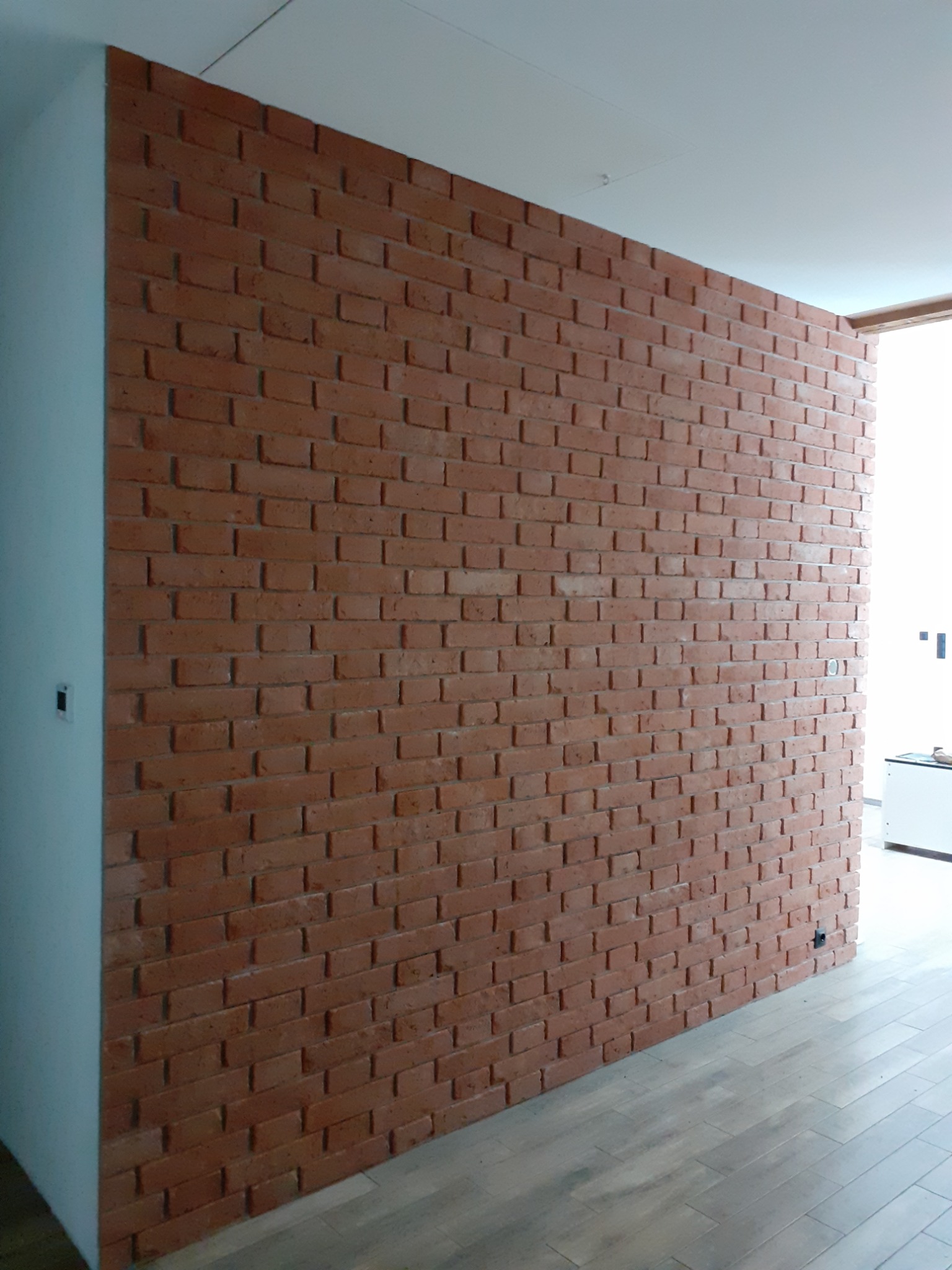 Dekoracyjna ściana z cegły klinkierowej w nowocześnie wykończonym wnętrzu, z widoczną częścią parkietu i fragmentem białej ściany.