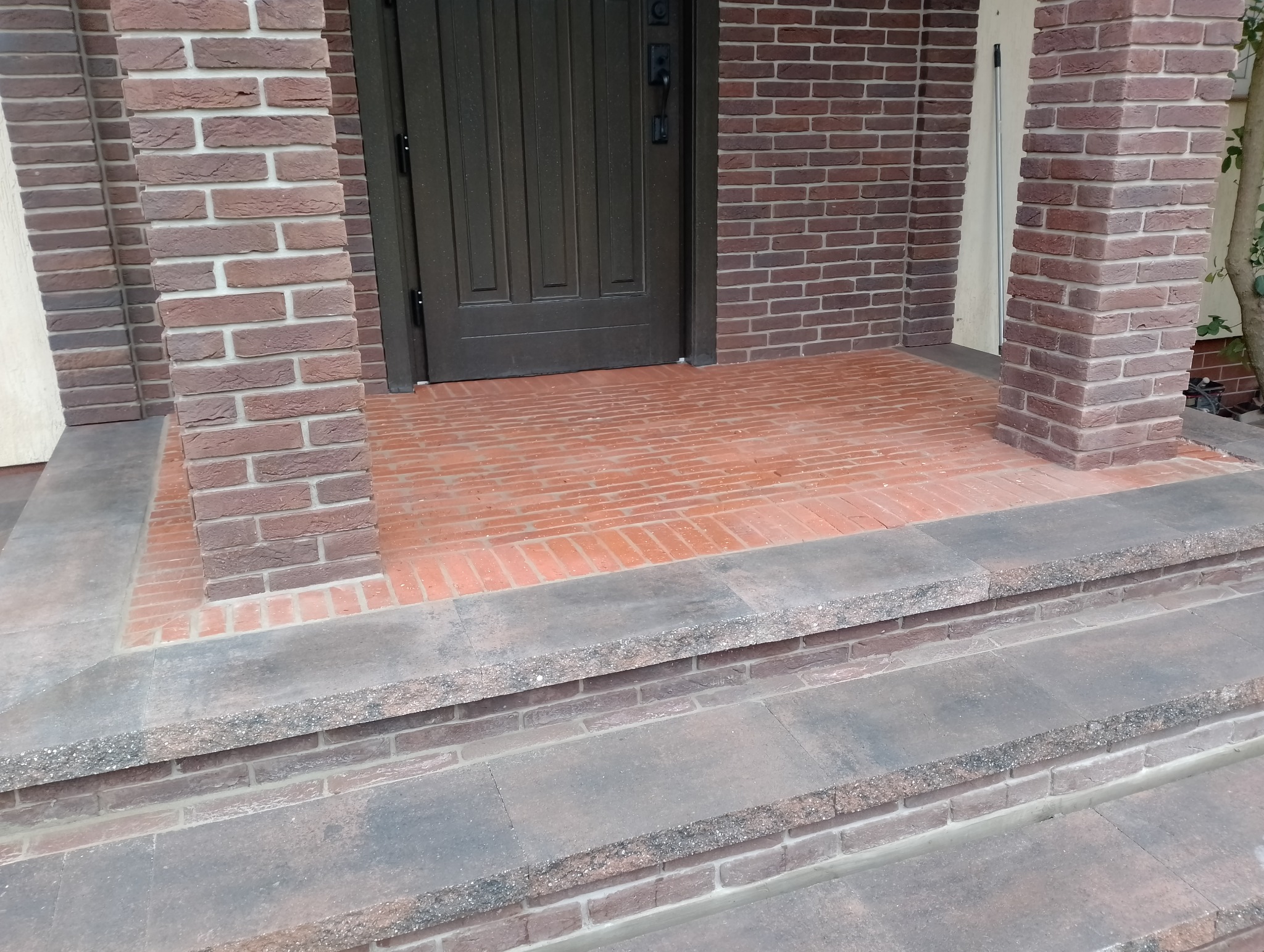 Wykończone wejście do domu z ceglaną elewacją i schodami wyłożonymi płytami z szarego kamienia.