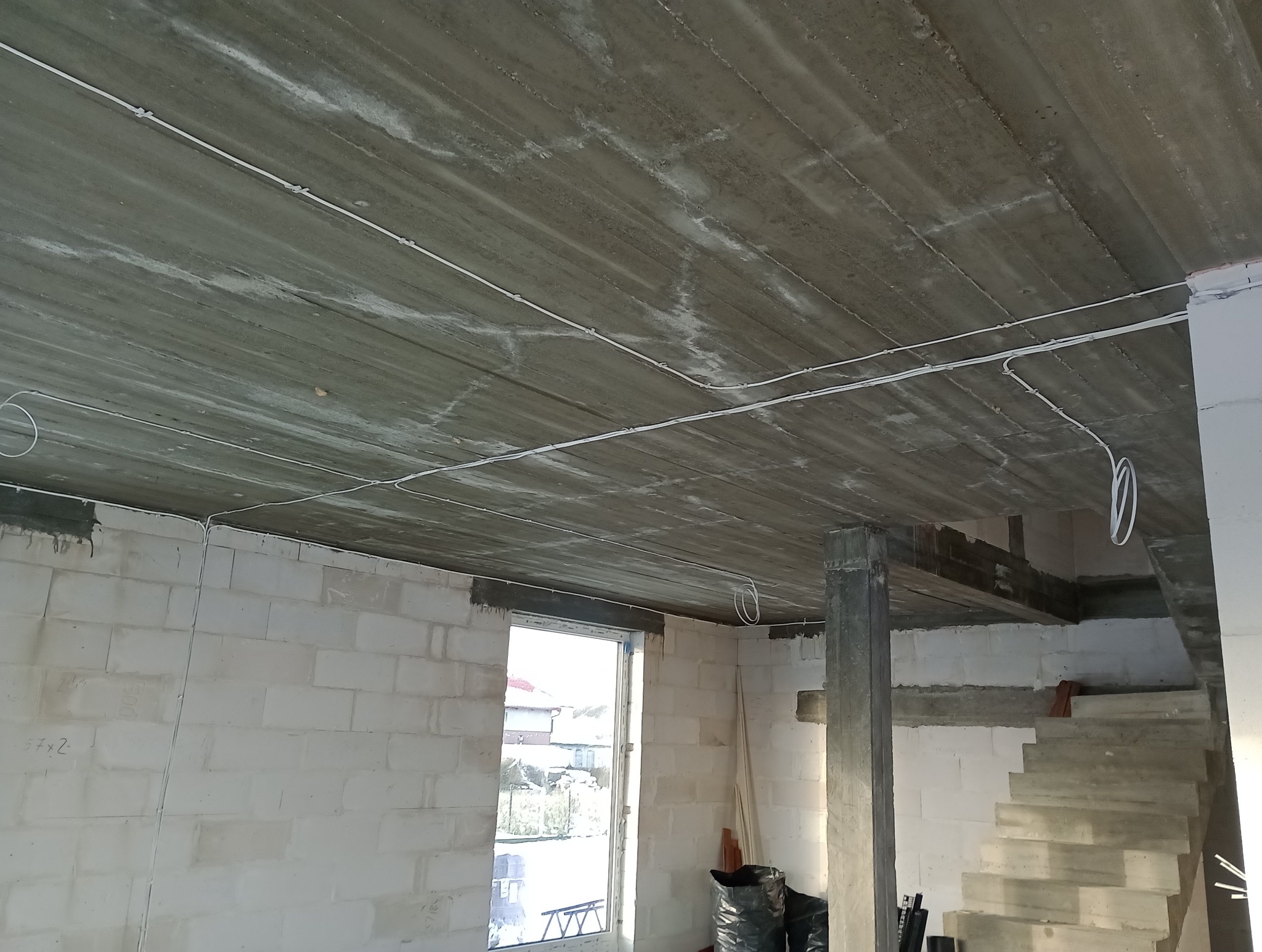 Surowy betonowy strop z widocznymi przewodami elektrycznymi, zamocowanymi klamrami, w trakcie prac wykończeniowych budynku.