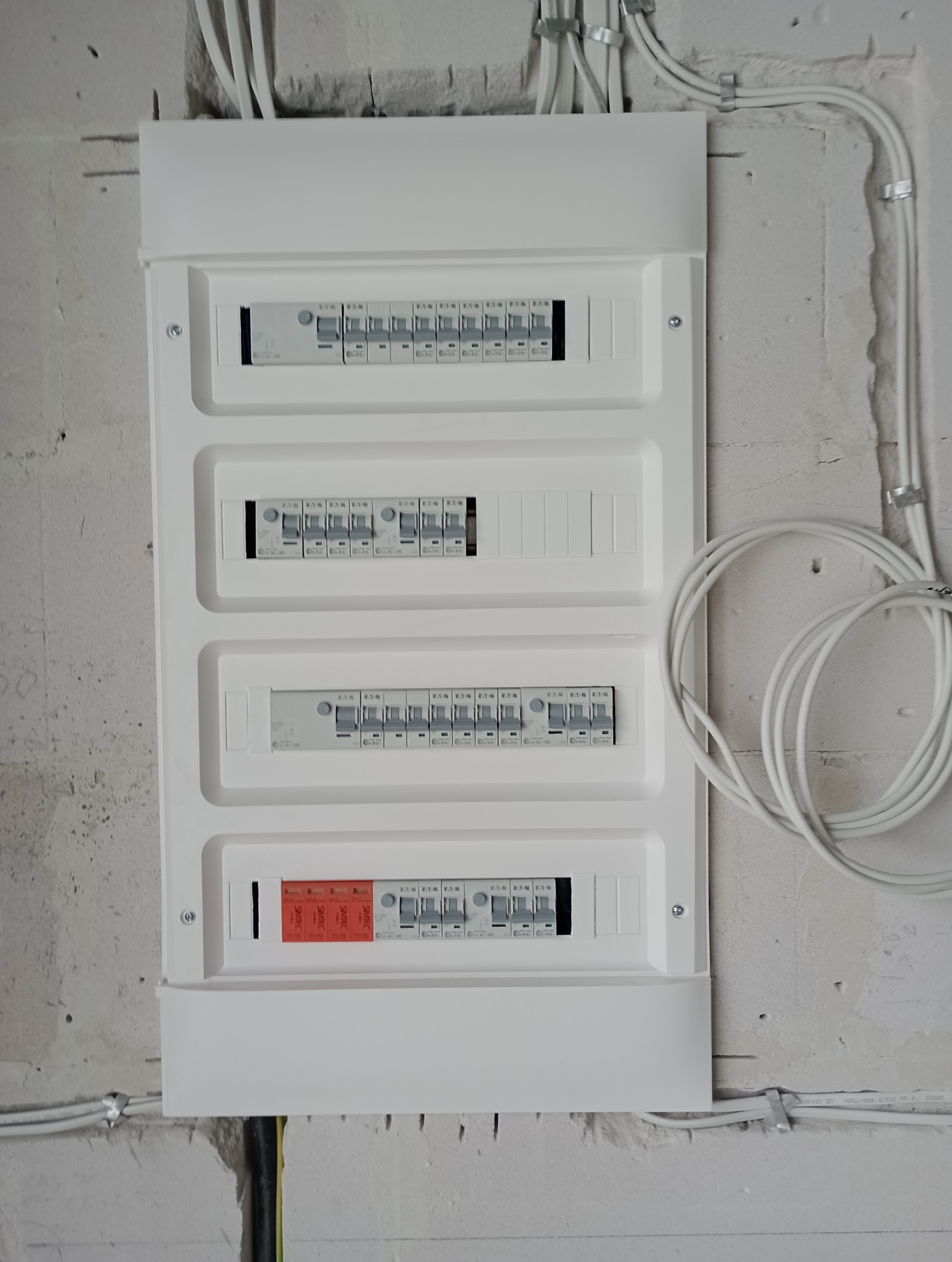 Biała skrzynka rozdzielcza z zamontowanymi bezpiecznikami i przewodami elektrycznymi na surowej ścianie z betonu komórkowego.