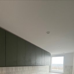 PHU POOLKRING Agnieszka Zenker - Nowoczesna kuchnia z oliwkowymi szafkami pod sufitem i białymi, podłużnymi płytkami na ścianie. Widok na okno z zielenią w tle. Minimalistyczny design.