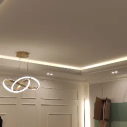 Wykończony sufit podwieszany z oświetleniem LED, nowoczesna lampa wisząca, ściana z dekoracyjnymi panelami i fragmentem marmurowej okładziny, widoczne ślady prac wykończeniowych.