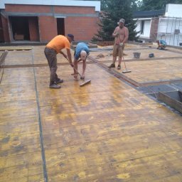 GRINKOR Sp. zo.o - Trzech robotników zamiata deskowanie szalunkowe pod wylewkę stropu na budowie domu murowanego, widoczne zbrojenie i fragmenty ścian.