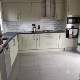 Krzysztof Zarski - Jasna kuchnia z frontami w stylu angielskim, czarnym blatem i białymi płytkami metra, wykończona stalowym okapem i piekarnikiem z mikrofalówką.