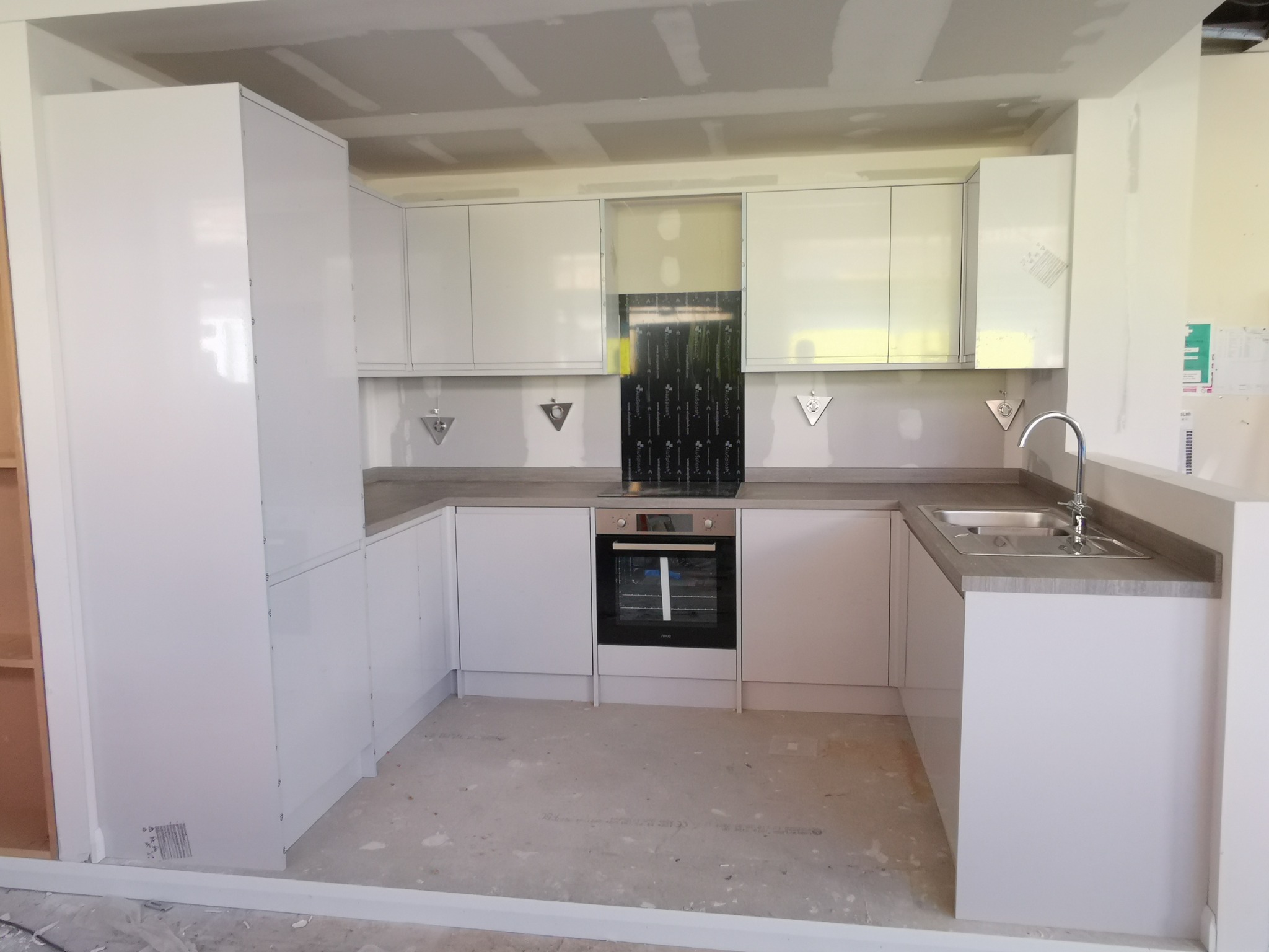 Montaż białej, nowoczesnej kuchni z szarym blatem w surowym stanie, widoczne płyty kartonowo-gipsowe na suficie i ścianach.