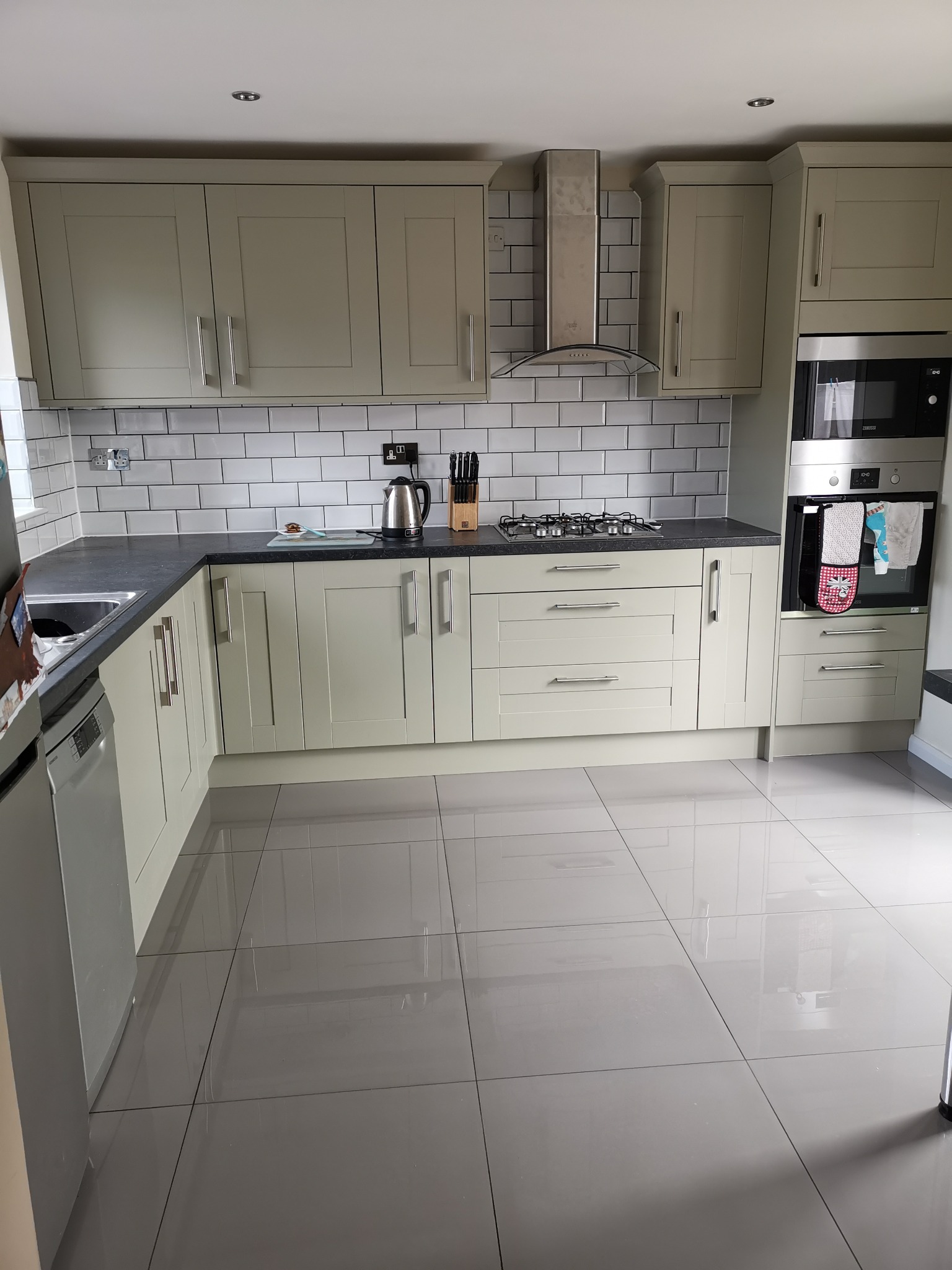 Jasna kuchnia z frontami w stylu angielskim, czarnym blatem i białymi płytkami metra, wykończona stalowym okapem i piekarnikiem z mikrofalówką.