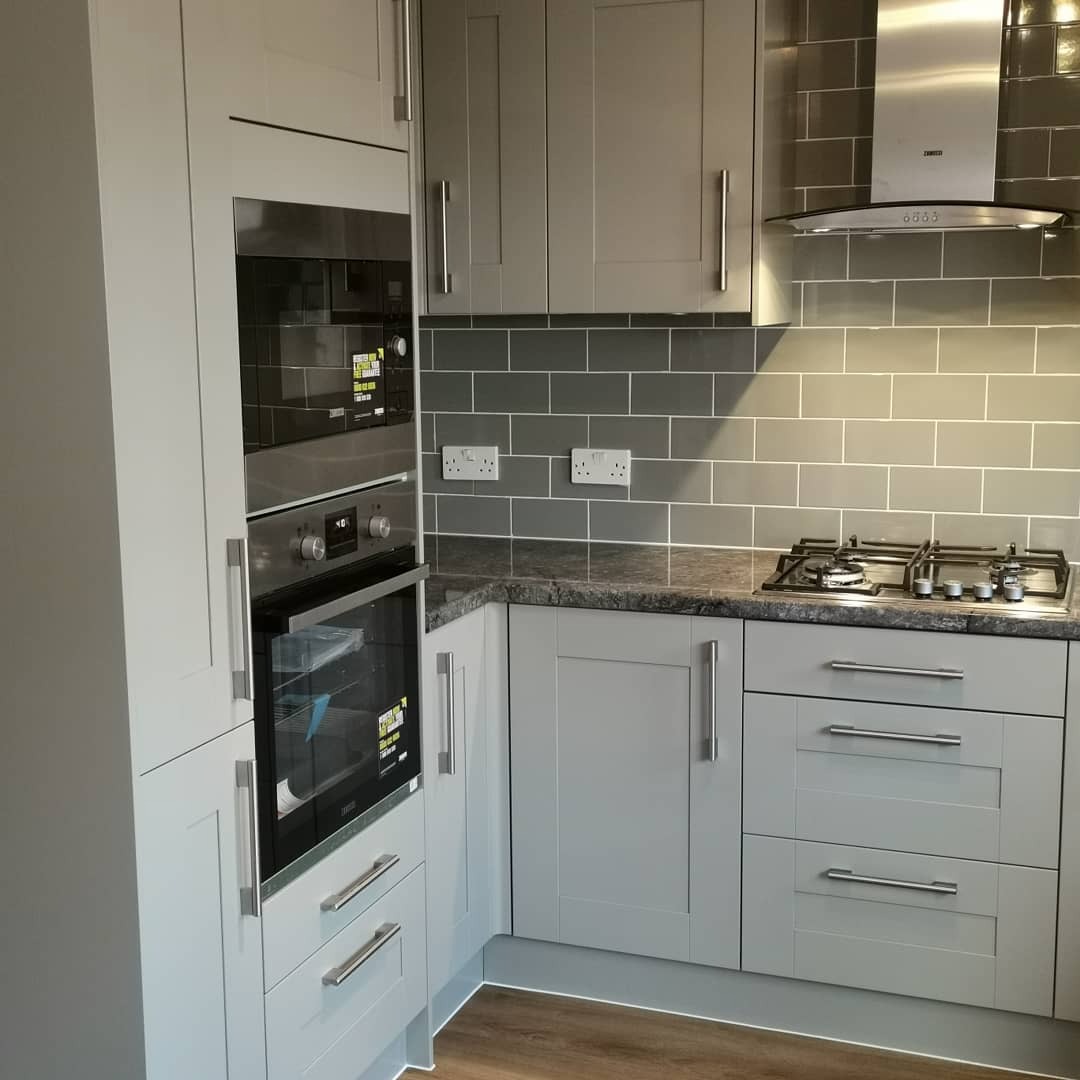 Szara kuchnia z zabudową piekarnika i kuchenką gazową, szare płytki na ścianie, stalowy okap, drewniana podłoga.