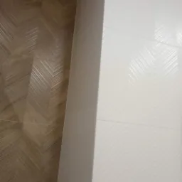 Fragment ściany z ułożonymi płytkami w jodełkę: brązowe płytki imitujące drewno po lewej i białe płytki z delikatnym wzorem po prawej stronie.