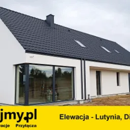 Nowoczesny dom jednorodzinny z białymi ścianami i ciemną dachówką, widoczna betonowa mieszarka i teren w trakcie zagospodarowywania.