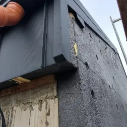 Nowoczesna, grafitowa obróbka blacharska dachu z rynnami, widoczne ocieplenie budynku styropianem grafitowym, ujęcie z dołu.