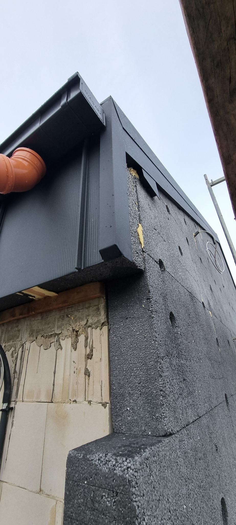 Nowoczesna, grafitowa obróbka blacharska dachu z rynnami, widoczne ocieplenie budynku styropianem grafitowym, ujęcie z dołu.