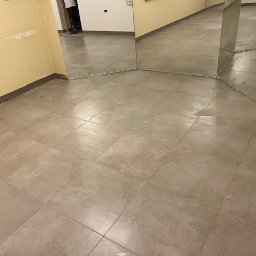 Yurii UWAGA! gładzi,malowanie. - Beżowe płytki podłogowe w pokoju z lustrami i fragmentem żółtej ściany. Widoczne fugi i listwy przypodłogowe. Ujęcie z niskiej perspektywy.