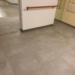 Yurii UWAGA! gładzi,malowanie. - Ułożone szare płytki podłogowe w łazience, widoczne lustro i grzejnik drabinkowy. Minimalistyczny design z drewnianym akcentem.