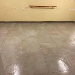 Yurii UWAGA! gładzi,malowanie. - Beżowe, kwadratowe płytki podłogowe z widoczną okrągłą plamą po środku, ściany w odcieniach żółci z widocznymi śladami po usuniętych elementach. Widok z perspektywy wejścia.