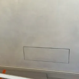 Ściana z dekoracyjną, srebrzystą gładzią wenecką, z ukrytym otworem rewizyjnym. Listwa przypodłogowa w dolnej części kadru.