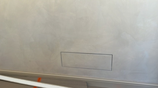 Ściana z dekoracyjną, srebrzystą gładzią wenecką, z ukrytym otworem rewizyjnym. Listwa przypodłogowa w dolnej części kadru.