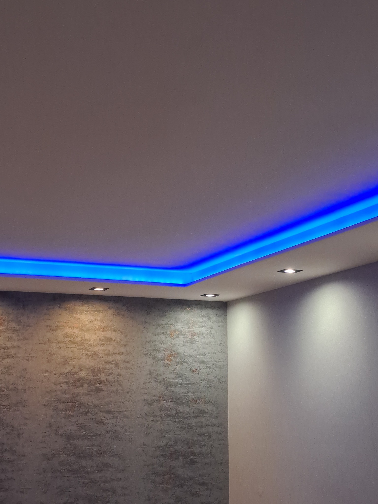Sufit podwieszany z niebieskim oświetleniem LED, dekoracyjna ściana z efektem betonu, reflektory punktowe