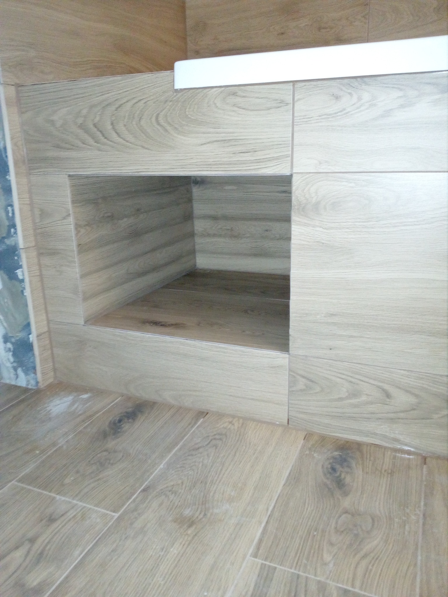 Wykończona wnęka w ścianie, obłożona płytkami imitującymi drewno, z dopasowaną podłogą. Widoczne niedociągnięcia przy łączeniu płytek na ścianie po lewej stronie.