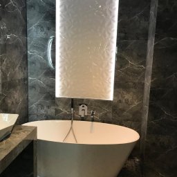 ŁazienkiSV - Nowoczesna łazienka z wolnostojącą wanną, szarymi marmurkowymi płytkami ściennymi i podświetlaną kolumną z białych płytek 3D, wzorzysta podłoga.