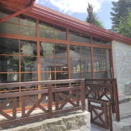 Duże okna z drewnianymi ramami w budynku z kamienną elewacją, widoczne z zewnątrz przez drewnianą balustradę.