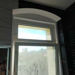 Waldek - Okno łazienkowe z zaokrąglonym nadprożem, widok na zewnątrz z zamazaną szybą, obok czarne płytki imitujące marmur