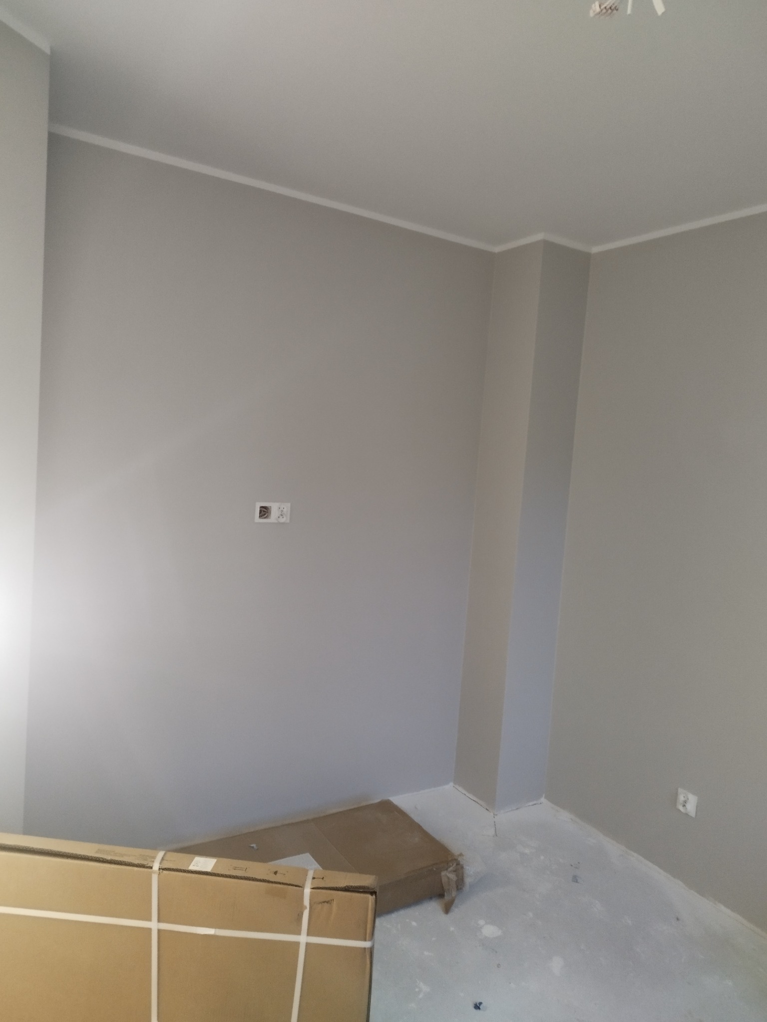 Świeżo pomalowane na szaro wnętrze pokoju z widocznymi listwami przypodłogowymi i kartonami na podłodze, przygotowane do dalszych prac wykończeniowych.