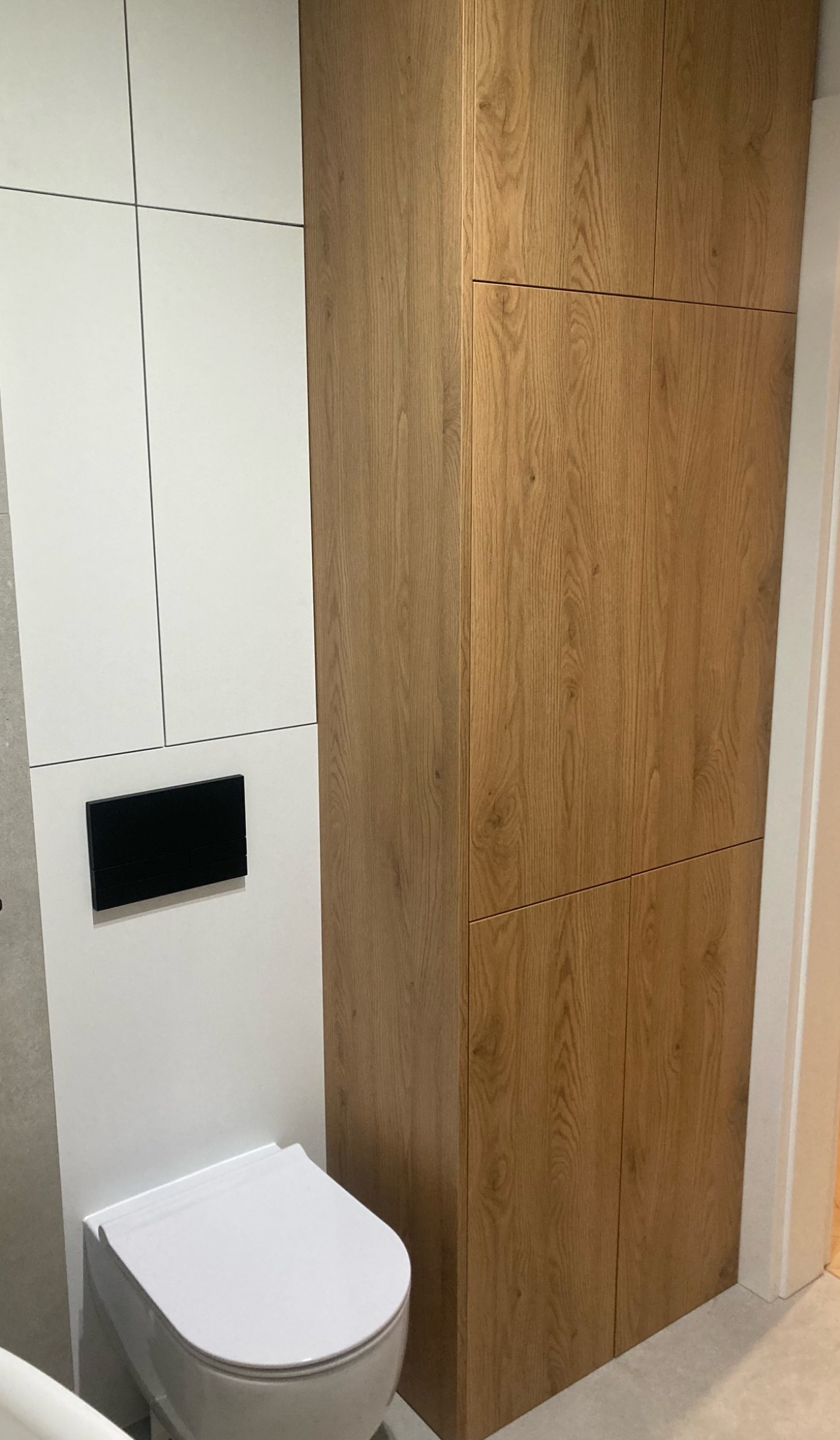 Nowoczesna łazienka z drewnianą zabudową szafkową, biała toaleta podwieszana i czarny panel sterujący.