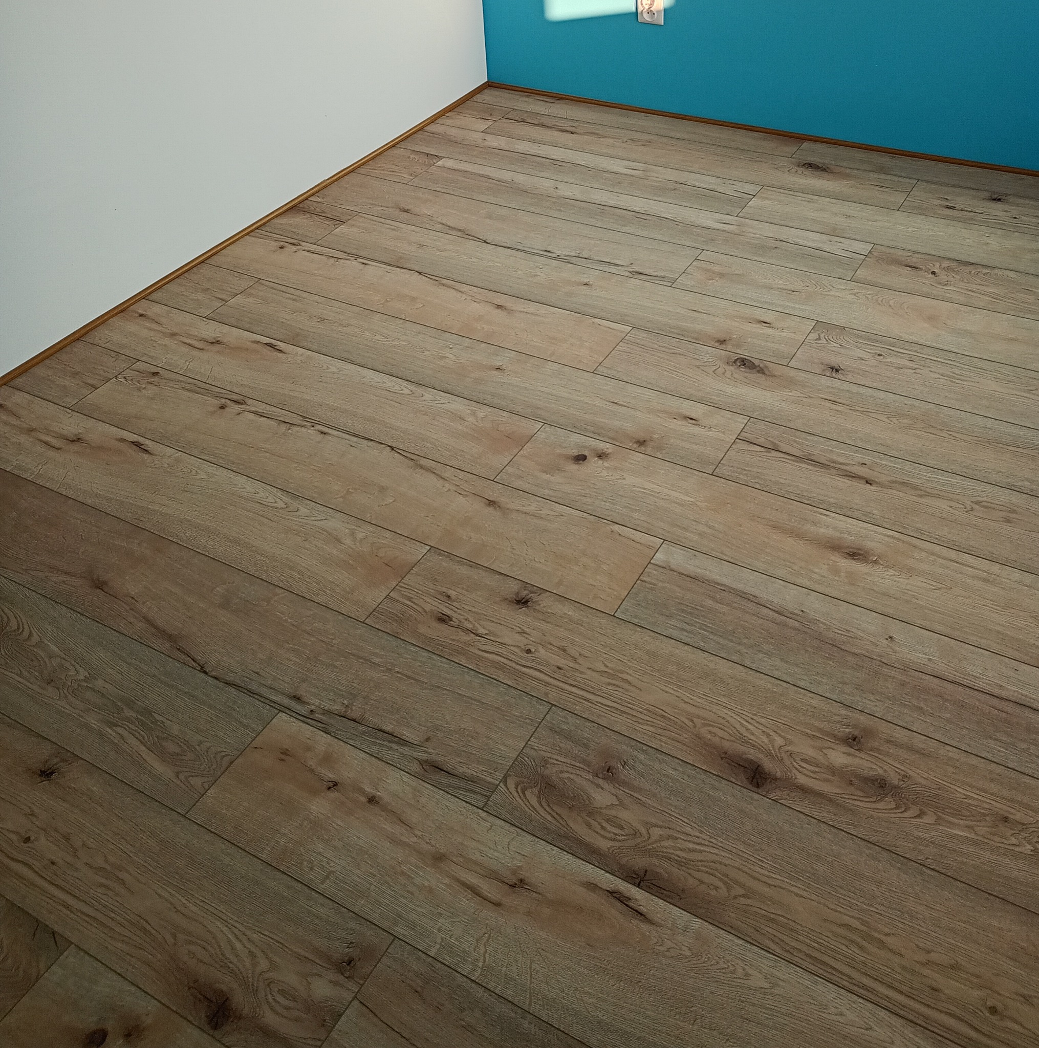 Ułożone panele podłogowe w rogu pokoju w Ustrzykach Dolnych. Widoczna listwa przypodłogowa i fragment ściany pomalowanej na biało i niebiesko.