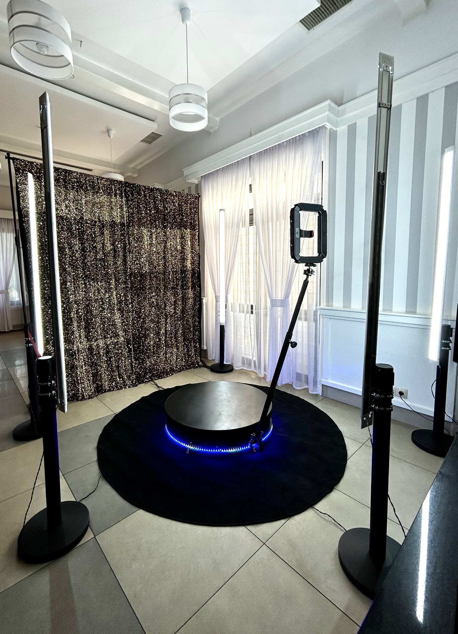 Okrągła platforma z niebieskim podświetleniem LED na czarnym dywanie, otoczona lampami pierścieniowymi i tłem z cekinami w jasnym pomieszczeniu.