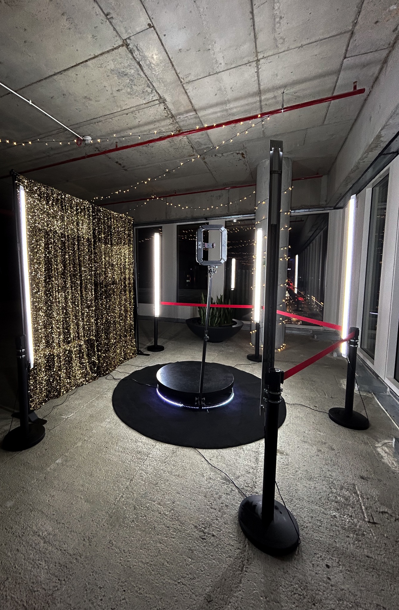 Kompletny, nowoczesny zestaw do zdjęć z obrotową platformą, oświetleniem LED i złotym, błyszczącym tłem, ustawiony w surowym, betonowym wnętrzu z oknami.